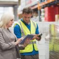 Manager using tablet while worker scanning package in warehouse